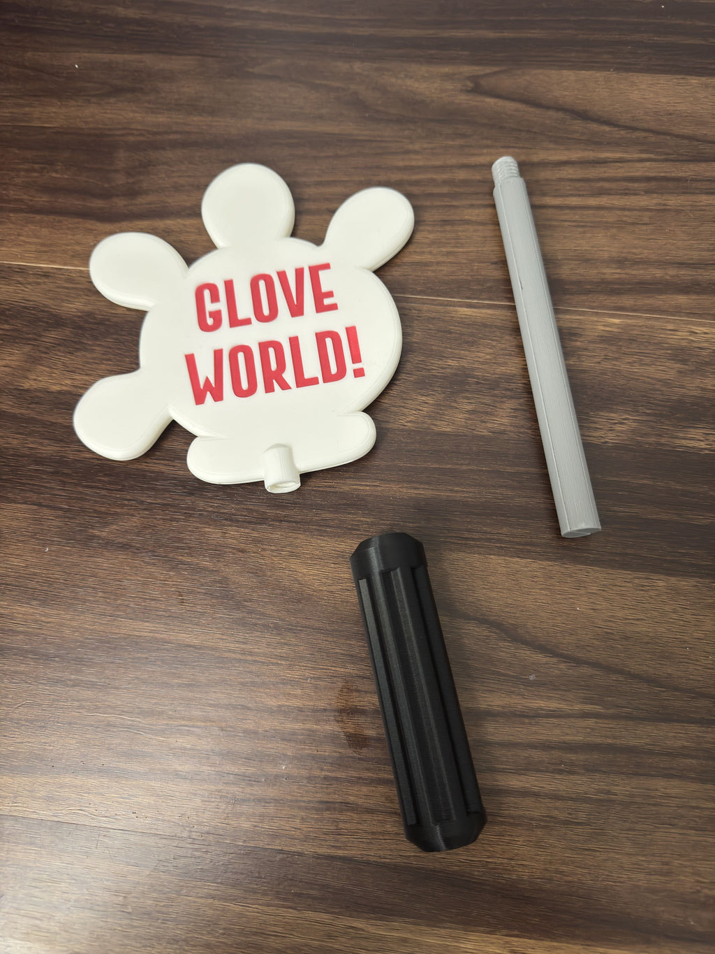 White toy Wand with 'Glove World!' text, accompanied by a gray rod and black cylindrical object.
